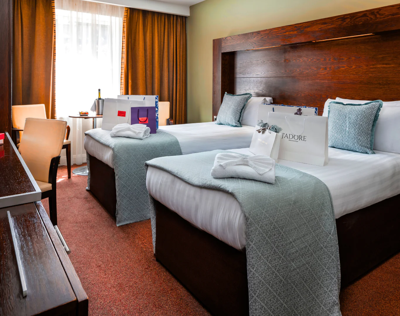 Elegant hotel room with twin beds, soft linens, gift bags, and a window view; ideal for a luxurious, relaxing stay.