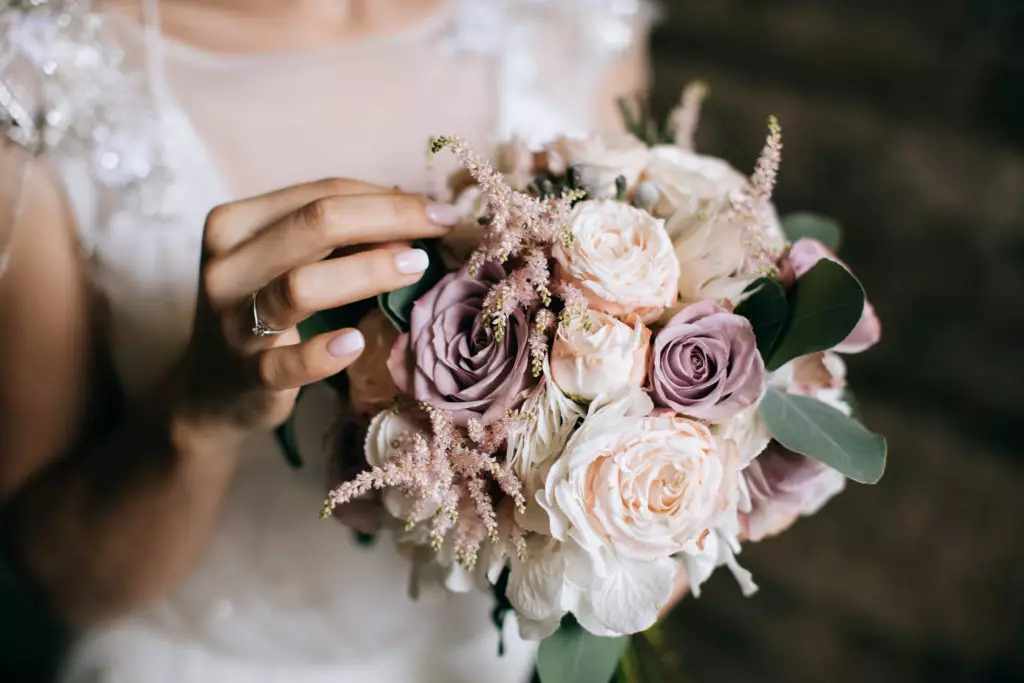 The bride holds a beautiful wedding bouquet of pink and white flowers in her hands