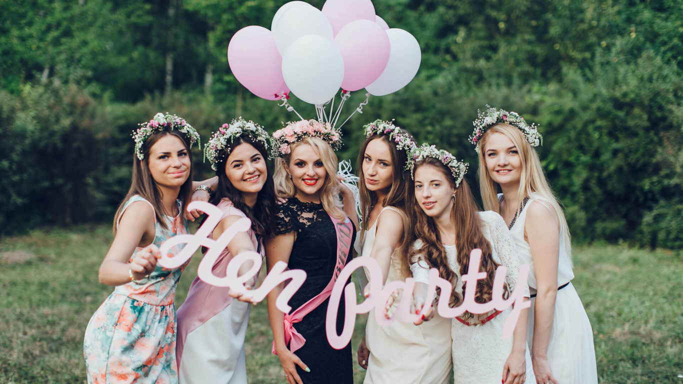 Hen party wearing flower crowns holding hen party sign and balloons