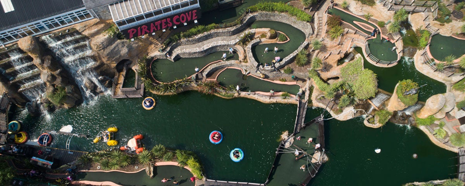 Aerial view of Pirate's Cove, showing winding crazy golf courses, several ponds with pedal boats, and landscaped waterfalls with people participating in activities.