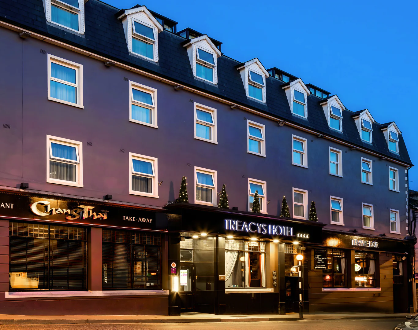 Cosy hotel exterior with welcoming lights, adjacent Thai restaurant, ideal for evening relaxation and local dining.