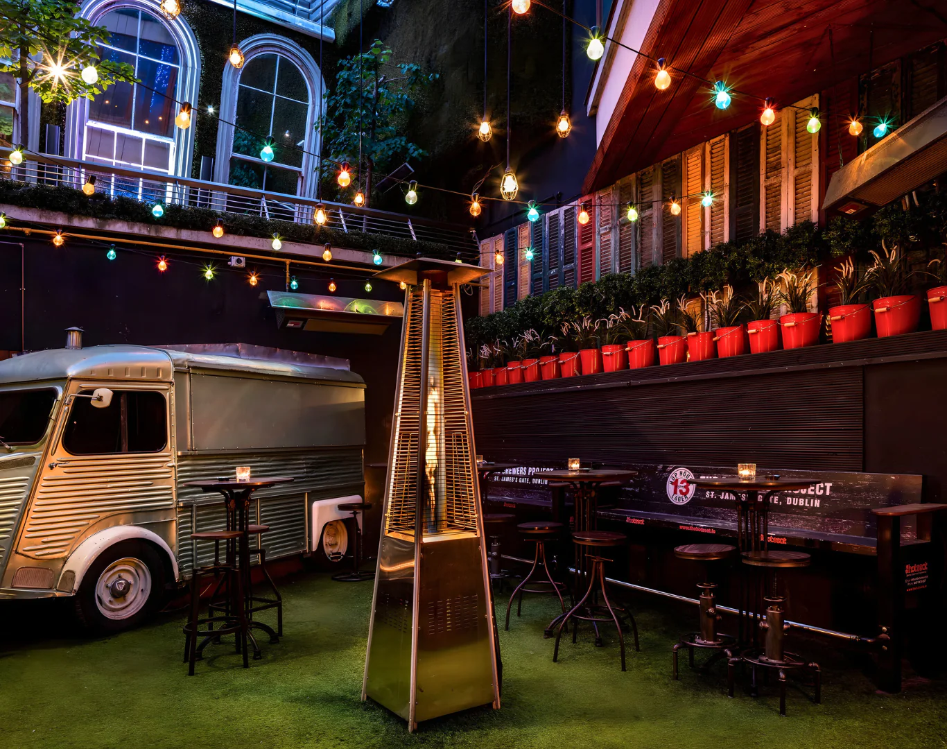 Charming courtyard with vintage van, vibrant lights, and cosy seating. Ideal for relaxing evenings in city hotel.
