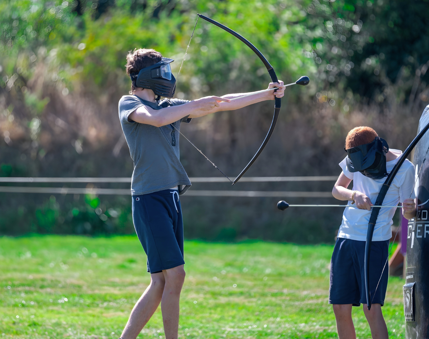 Guests enjoying an exciting archery game on lush hotel grounds, featuring protective gear and bows for a fun outdoor experience.