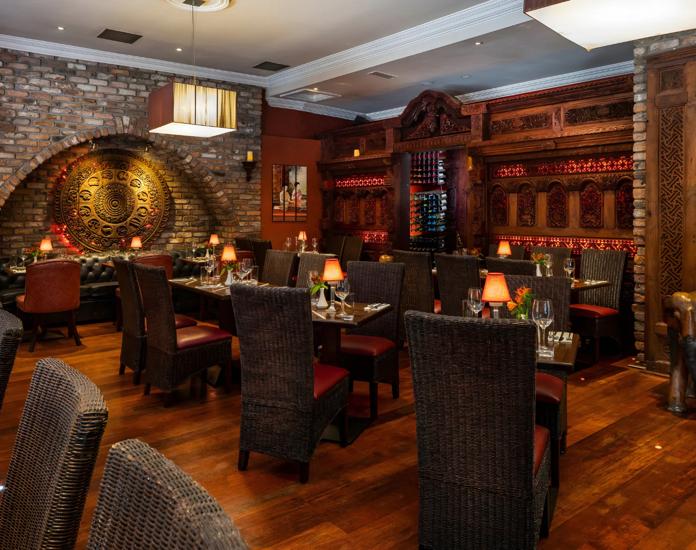 Elegant restaurant with rich wood décor, soft lighting, plush seating, and a wine display, offering a warm dining experience.