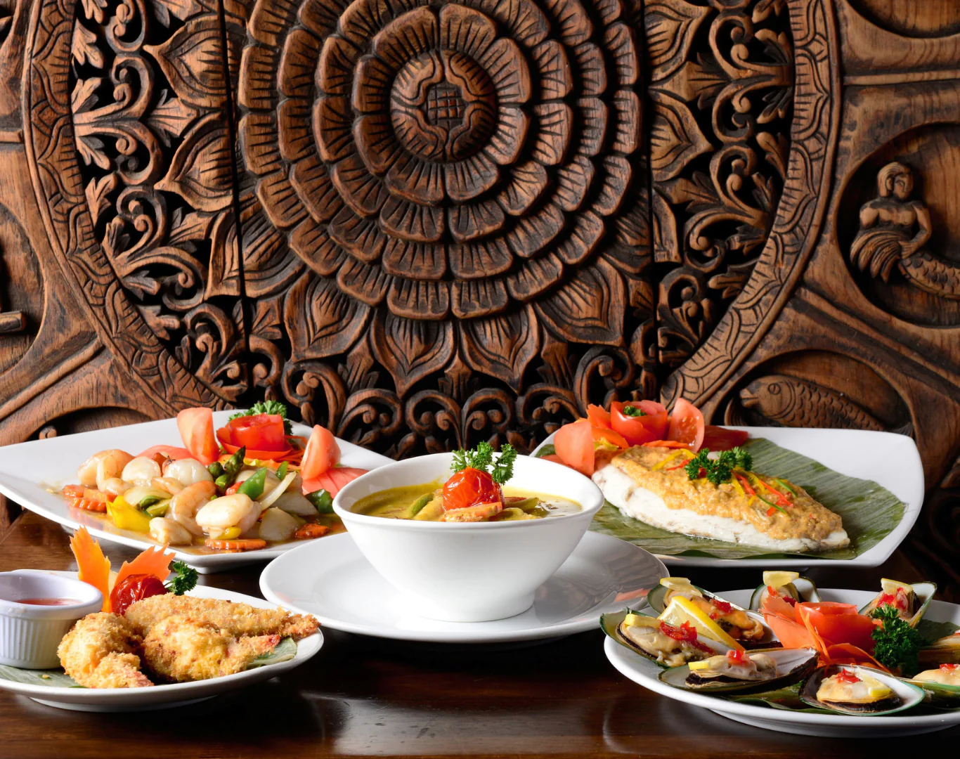 Delectable cuisine in front of intricate carved wood, featuring fresh seafood and vibrant vegetables, inviting dining experience.