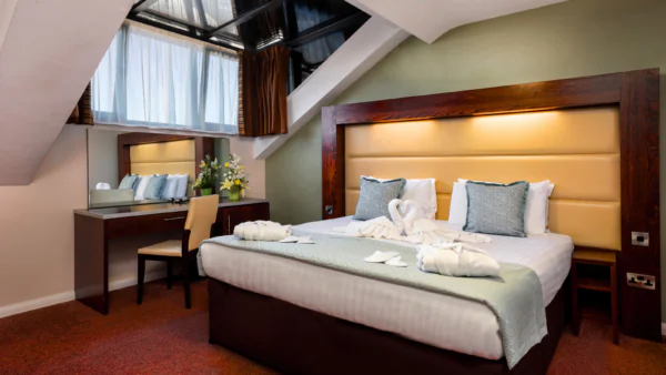 Elegant hotel room with plush king bed, decorative swan towels, stylish vanity, and skylight for a luxurious stay.