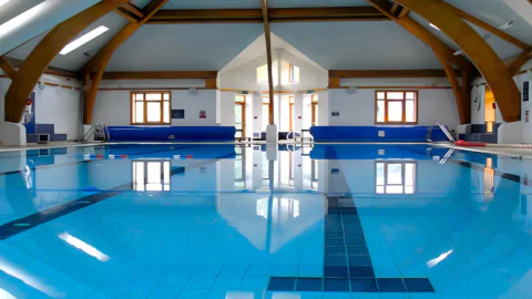 Serene indoor pool with wooden beams and skylights, offering a calming swim experience at luxury hotel.