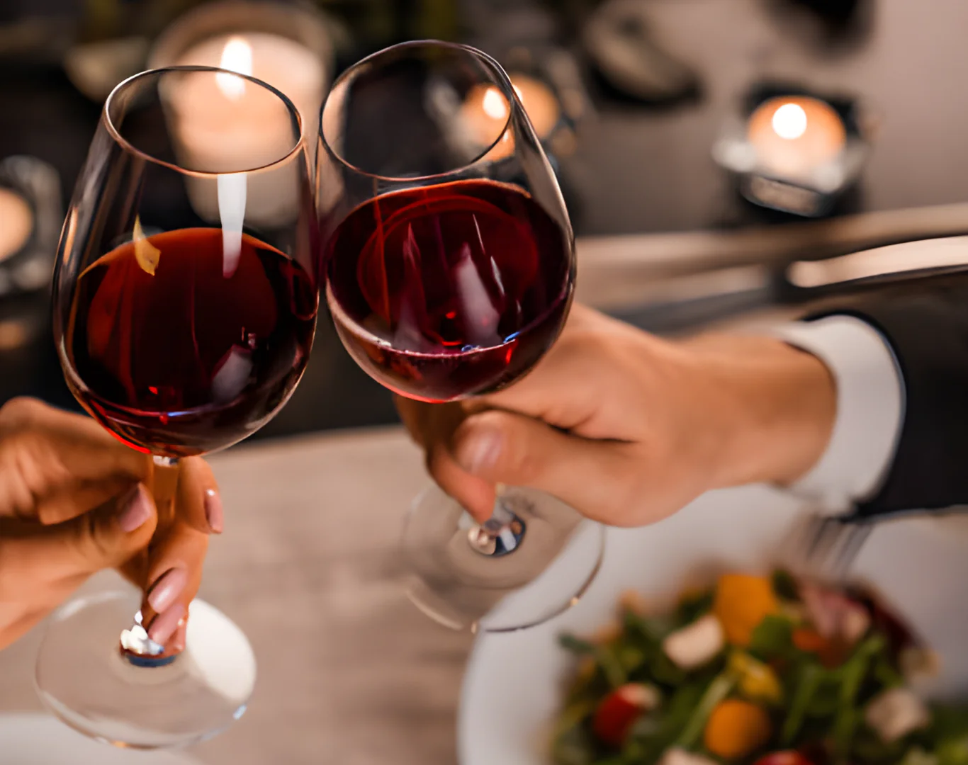 Guests toasting red wine in an elegant candlelit hotel restaurant, enjoying a gourmet salad for a romantic dining experience.