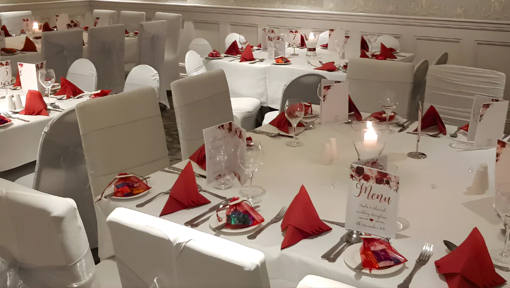 Elegant banquet hall set for an intimate wedding, featuring candlelit tables, white chairs, and vibrant red accents.