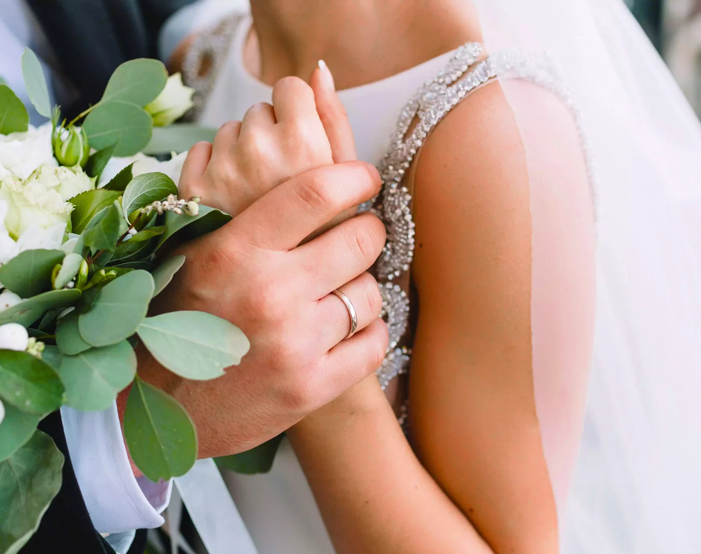 Elegant couple holding hands, bride with bouquet of white roses; romantic wedding venue at luxurious hotel.