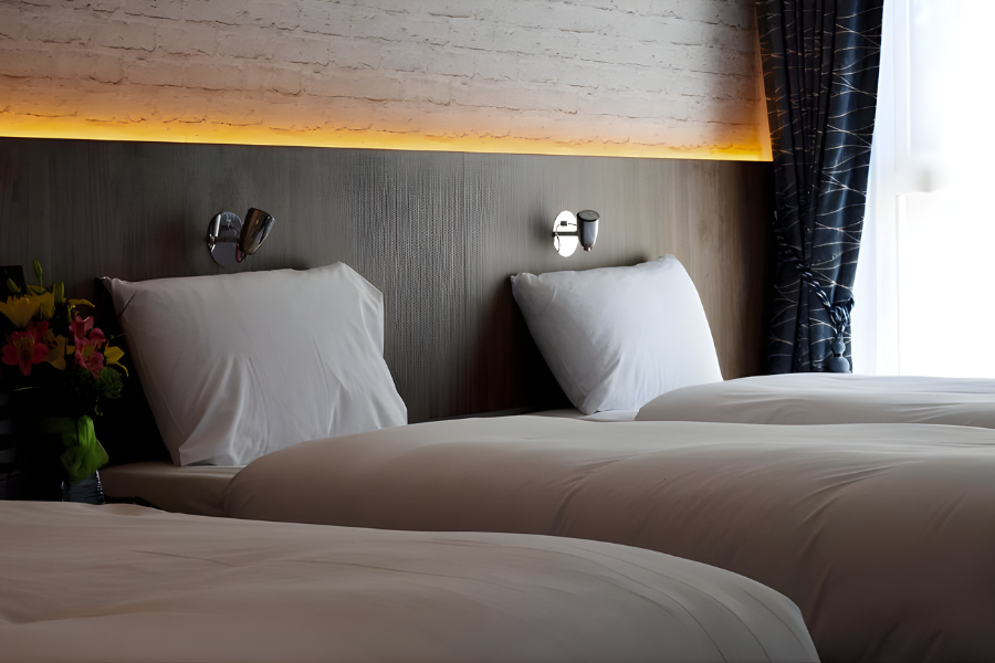 Elegant hotel room with cosy twin beds, soft lighting, and plush pillows for a restful stay near city centre attractions.